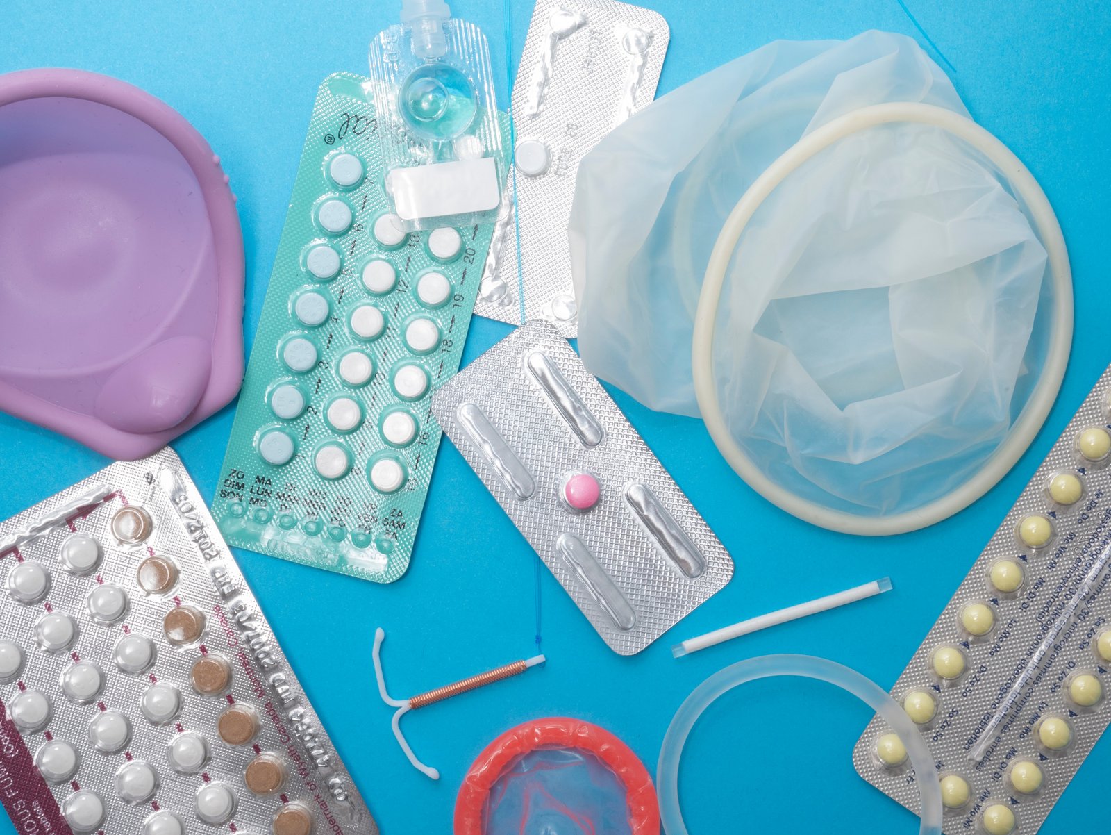 Een blauwe achtergrond waarop verschillende hormonale en hormoonvrije anticonceptiemiddelen voor vrouwen liggen