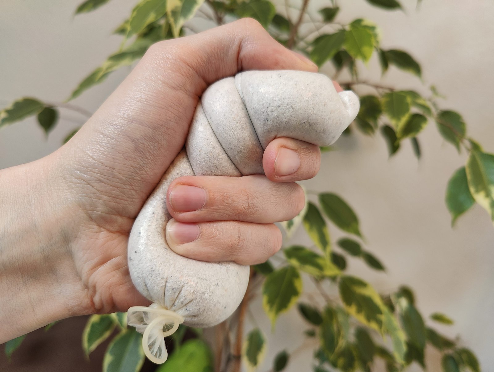 Een verlopen condoom gevuld met zand, in de hand van iemand die het als stressbal gebruikt